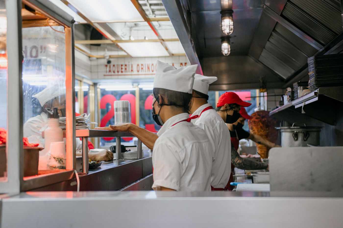 Cooks in caps and face masks working a compact counter kitchen