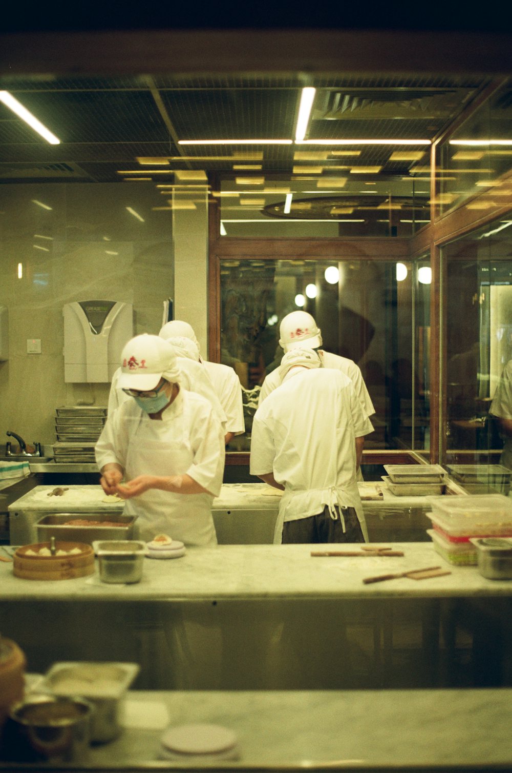 Masked chefs in whites and caps preparing food in a large, well-lit kitchen
