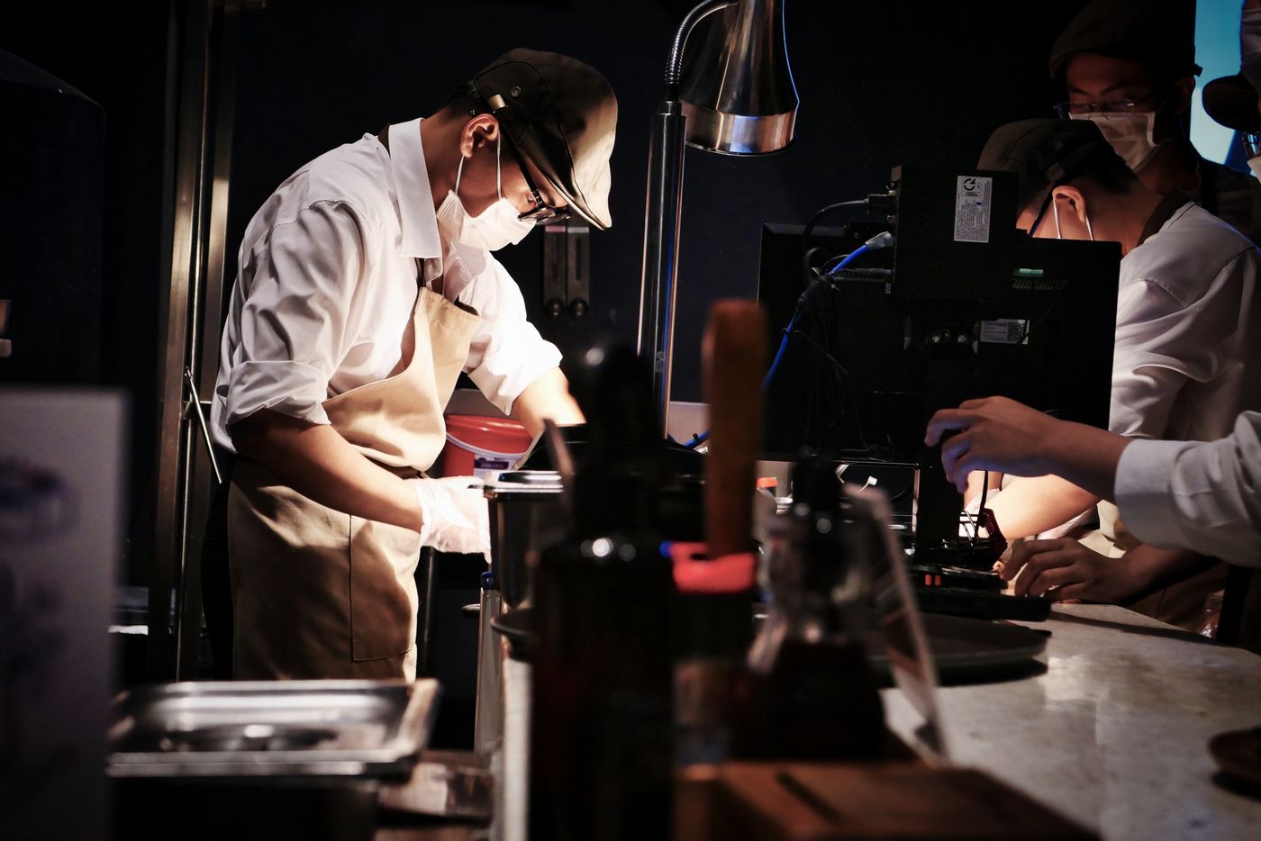 Chefs in face masks and aprons preparing dishes during service in a restaurant kitchen