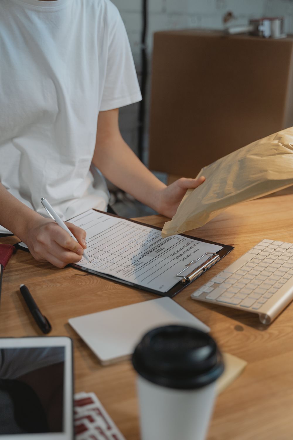 A person filling in a form on a clipboard at a wooden work table