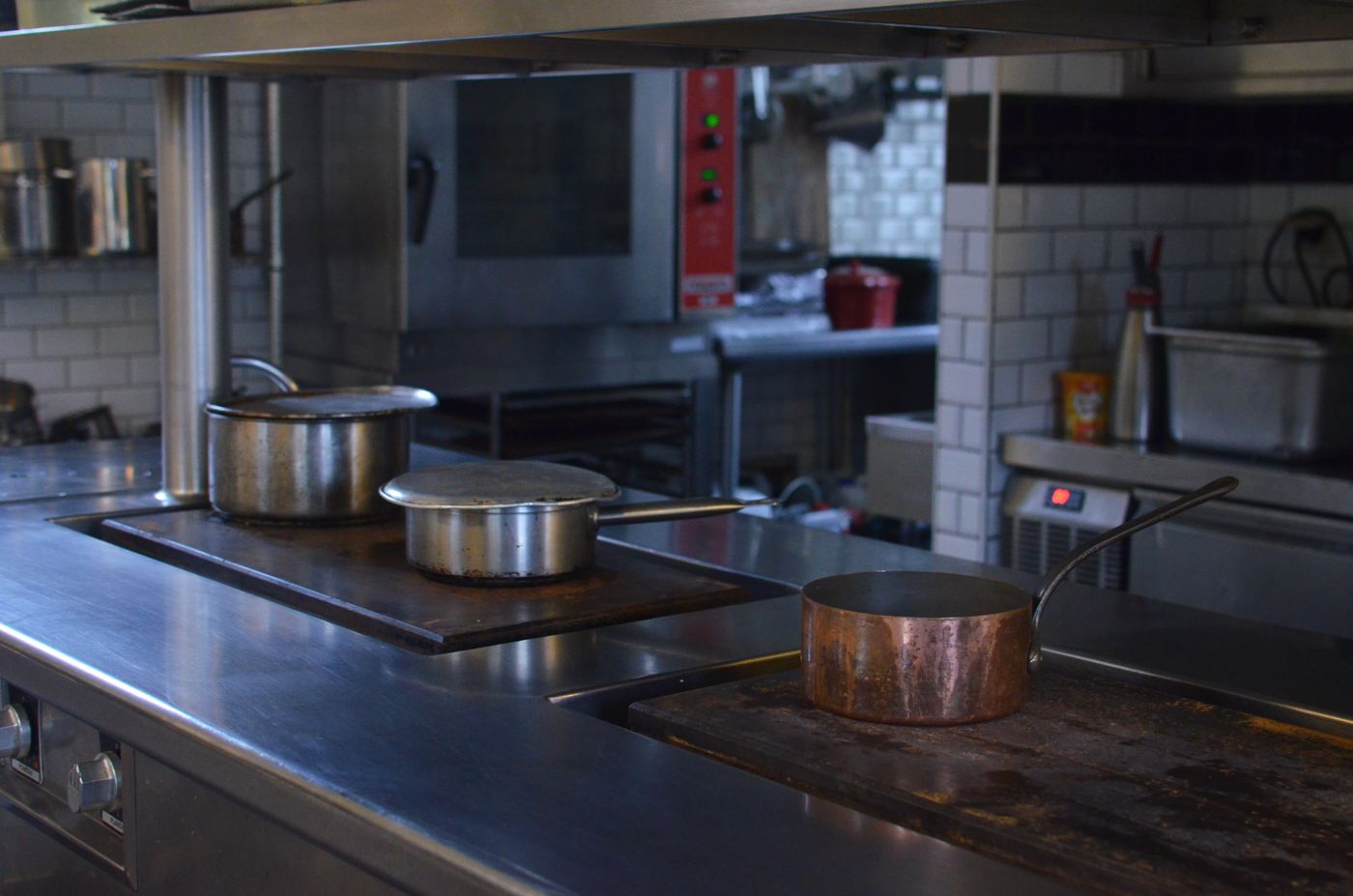 A clean stainless-steel cooking station with pots and a copper pan in a professional kitchen